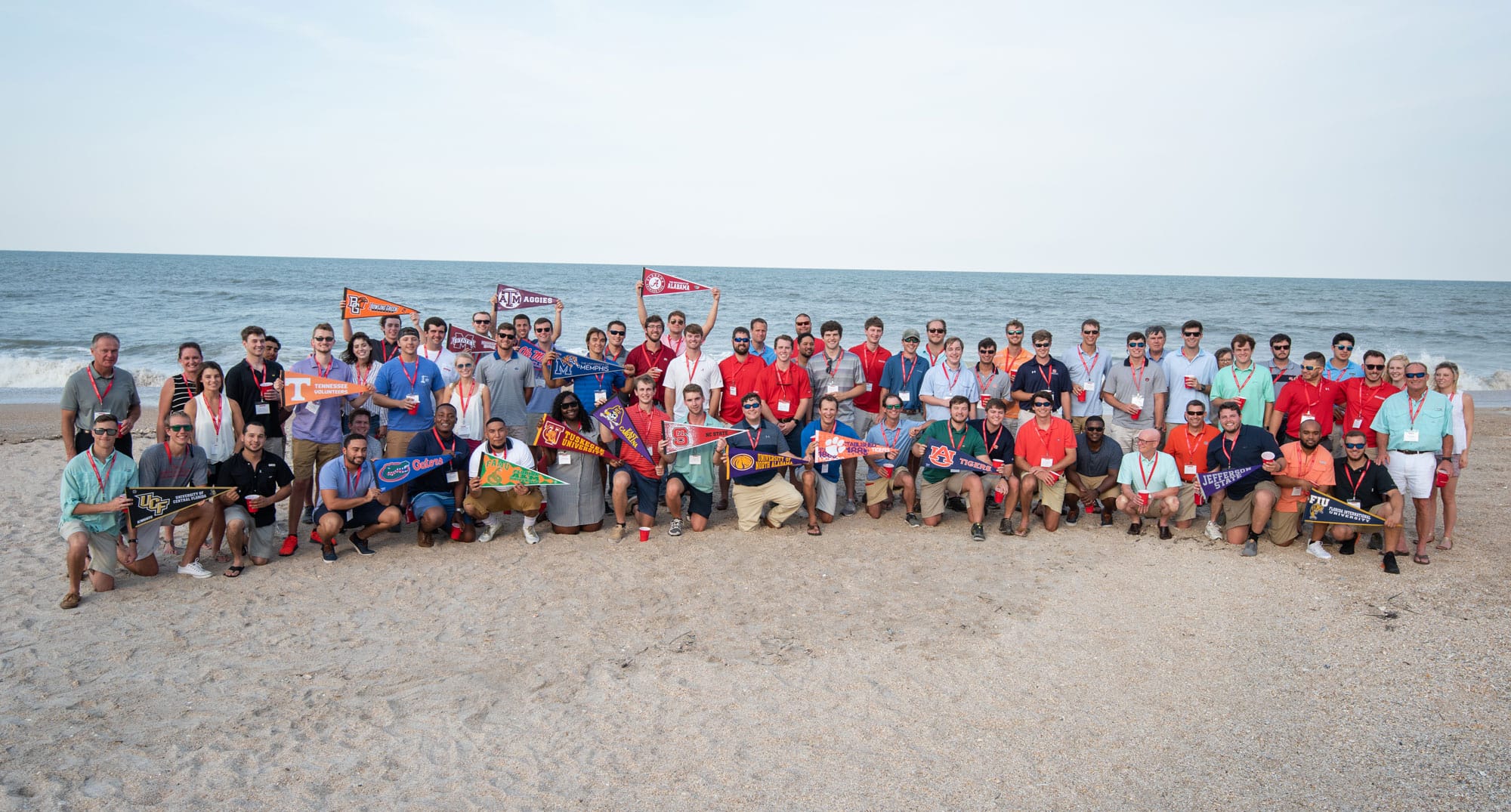 interns and staff at the beach holding college flags